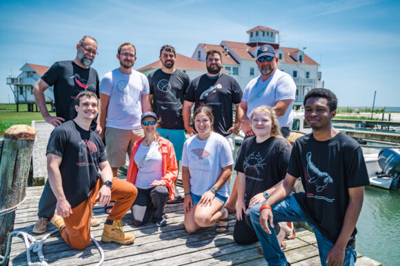 Researchers, technicians and students model the Rutgers Marine Field Station 50th anniversary special collection t-shirts. Back row (l. to r.): Research associate professor Thomas Grothues, laboratory technician Douglas Hood, marine field technician Ryan Scully, marine field technician Scott Pescatore, laboratory researcher Roland Hagan Front row (l. to r.): Salvatore Fricano (SEBS ’23), PhD candidate Carolyn Iwicki (SEBS), laboratory assistant Miranda Rosen, marine field technician Kieran Bates, Jamin Brako (SOE ’25)